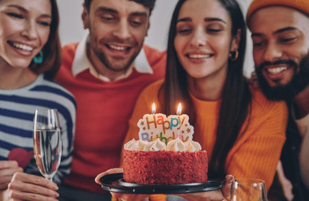 Beautiful young people holding birthday cake and smiling while celebrating together