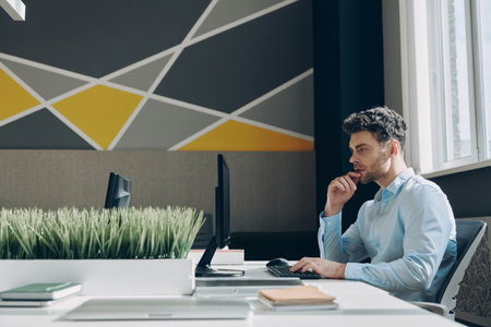 Concentrated young businessman using computer while sitting at his working place in officeの写真素材
