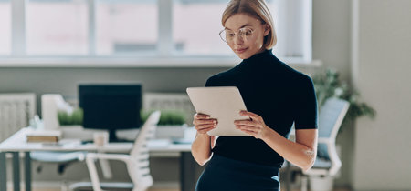 Confident businesswoman using digital tablet while standing near her working place in office