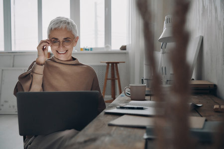 Confident senior businesswoman using laptop and smiling while sitting at her working placeの写真素材