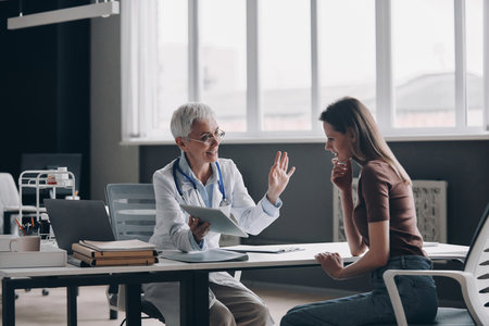 Confident female doctor talking to patient and smiling while sitting at the office togetherの写真素材
