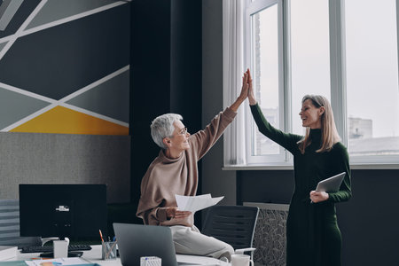 Two happy women giving high five to each other while standing in the office together