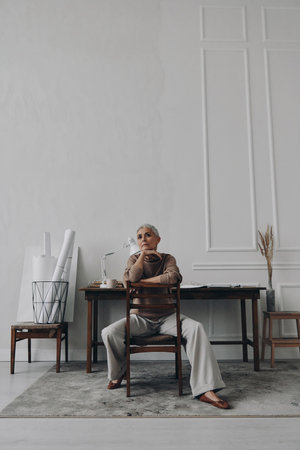 Thoughtful senior woman holding hand on chin while sitting at her creative working placeの写真素材