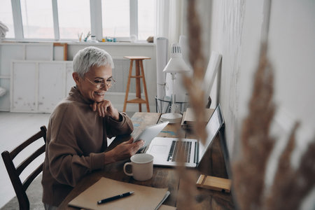 Happy senior businesswoman using digital tablet while sitting at her working placeの写真素材