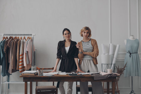 Two confident female fashion designers looking at camera while standing in workshop togetherの写真素材