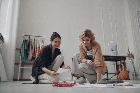 Two happy female fashion designers planning new collection in workshop together