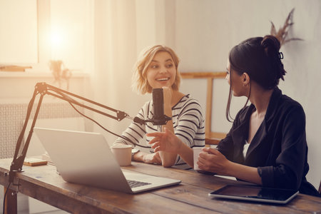 Two attractive young women communicating while providing live stream in studio togetherの写真素材
