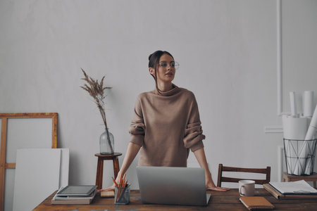 Beautiful young woman looking confident while leaning at the desk in creative officeの写真素材