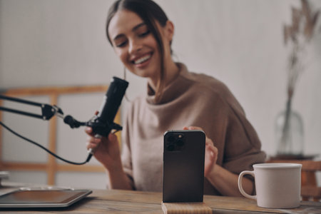 Happy young woman recording podcast while sitting at her workplace in studioの写真素材
