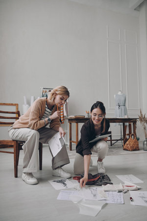 Two confident female fashion designers examining sketches while working in workshop