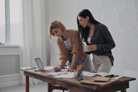 Two concentrated young female colleagues working with papers in the office togetherの写真素材