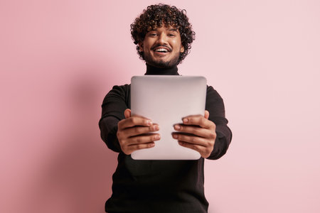 Handsome Indian man holding digital tablet and smiling against pink backgroundの写真素材