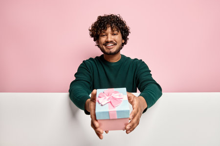 Handsome Indian man stretching out gift box against pink backgroundの写真素材