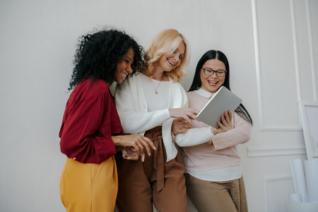 Three happy mature women using digital tablet while leaning on the wall togetherの写真素材