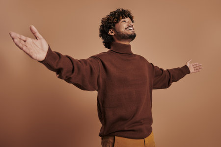Relaxed Indian man stretching out hand and smiling against brown backgroundの写真素材