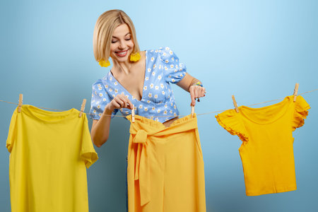 Beautiful young woman hanging her colorful clothes on clothesline against blue backgroundの写真素材
