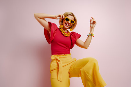 Playful young woman in vibrant clothes dancing and smiling against colored backgroundの写真素材