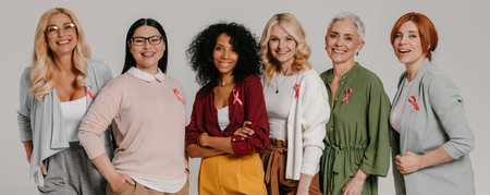 Group of mature women wearing breast cancer ribbons and smiling against grey backgroundの写真素材