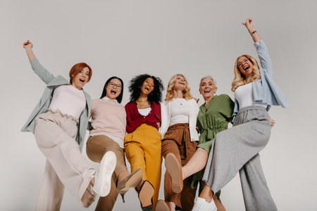 Multi-ethnic group of cheerful mature women embracing and dancing against grey backgroundの写真素材