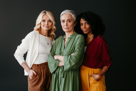 Three confident mature women looking at camera while bonding against grey backgroundの写真素材