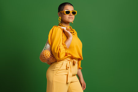 Fashionable young short hair woman carrying mesh bag with oranges against green backgroundの写真素材