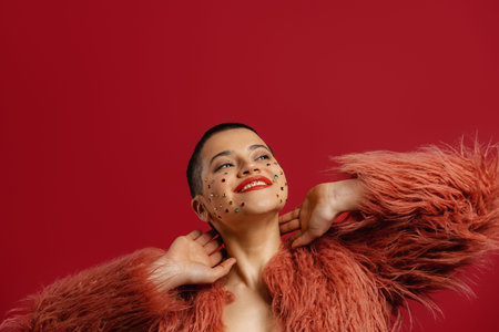 Happy young short hair woman with shiny crystals over her face standing against red backgroundの写真素材