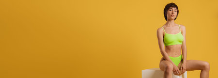 Attractive young short hair woman in underwear sitting against yellow backgroundの写真素材