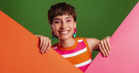 Joyful young woman looking out of the colorful banners while standing against background