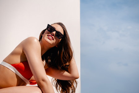 Beautiful young woman in bikini adjusting hair and smiling against white background outdoorsの写真素材