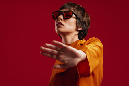 Attractive young short hair woman in trendy glasses stretching out hand against red background