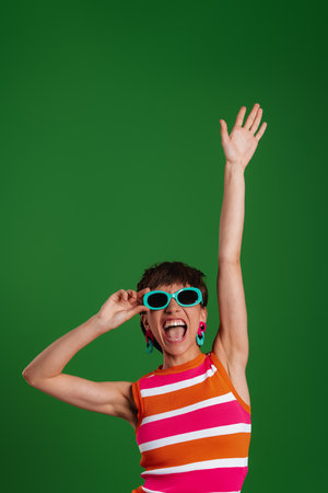 Happy young woman in trendy glasses gesturing while standing against green backgroundの写真素材