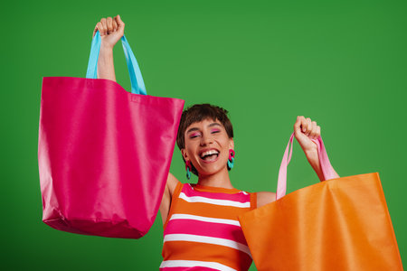 Excited young woman showing her colorful shopping bags while standing against green backgroundの写真素材