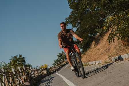 Confident young man riding bicycle by the scenic road outdoorsの写真素材
