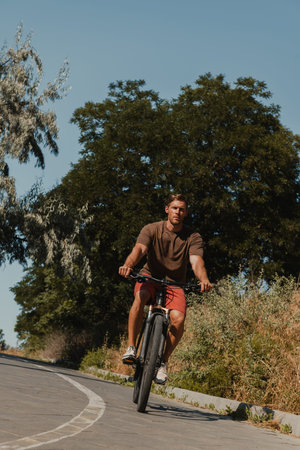 Confident young man riding bicycle by the scenic road outdoors