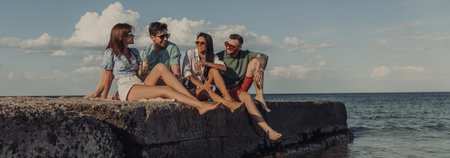 Group of happy young friends enjoying beer while spending carefree time seaside together
