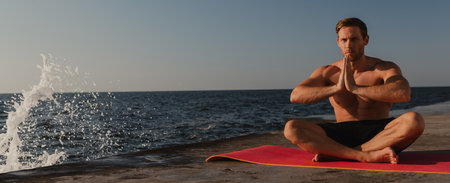 Confident young shirtless man practicing yoga while meditating near the sea at the morningの写真素材