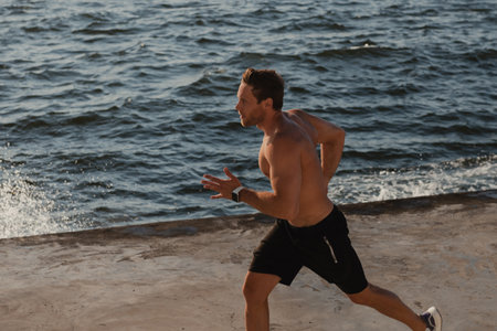 Top view of confident athletic man jogging by the pier with the sea on backgroundの写真素材