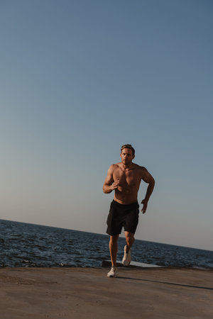 Confident athletic man jogging outdoors with the sea on background