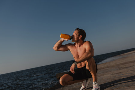 Confident male athlete drinking water while resting after morning training outdoorsの写真素材