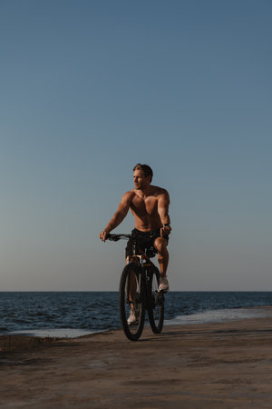 Handsome young shirtless man enjoying summer morning while cycling seasideの写真素材