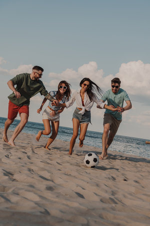 Group of happy young people spending carefree time together while playing beach soccerの写真素材