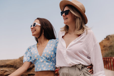 Two beautiful young women embracing and smiling while walking outdoors togetherの写真素材