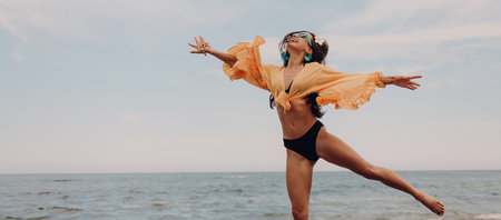 Joyful young woman in swimwear jumping while enjoying summer day on the beachの写真素材