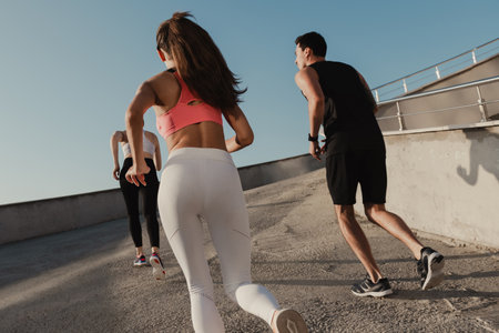 Rear view of three young people in sportswear running outdoors togetherの写真素材