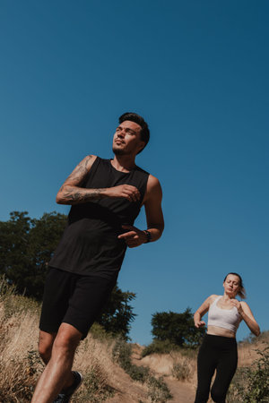 Concentrated young couple in sportswear running down by the footpath while training outdoors...