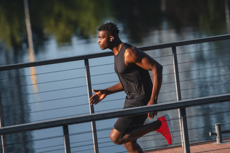 Concentrated young African man in sportswear running by the riverbank
