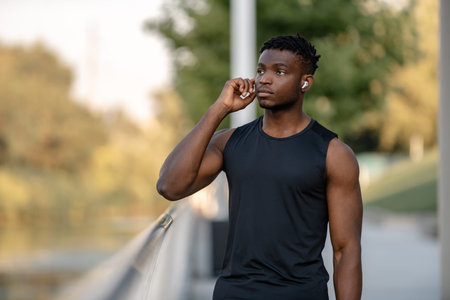 Cheerful African man in sportswear adjusting his headphones while resting during the training...