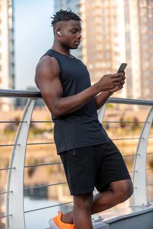 Young African man in sportswear checking his fitness program while using smart phone outdoorsの写真素材