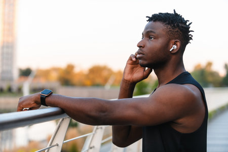 Handsome African man in sportswear adjusting his headphones while resting after training outdoorsの写真素材