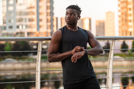 Handsome African man in sportswear using smart watch while having a break during the training...